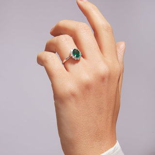 Hand wearing a ring with a green gemstone on a plain background
