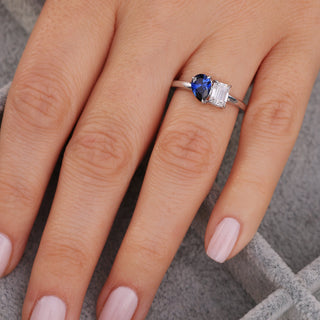 Silver ring with a blue gemstone on a person's finger against a neutral background