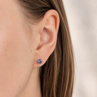 Close-up of an ear wearing a blue gemstone stud earring on a neutral background