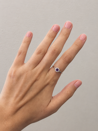 Hand wearing a ring with a purple gemstone on a neutral background