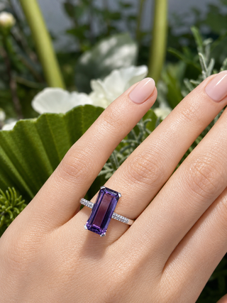 Hand wearing a purple gemstone ring with a natural background