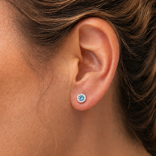 Close-up of an ear wearing a blue gemstone earring with brown hair.