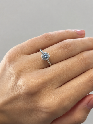 Hand wearing a white gold ring with a blue gemstone on a neutral background