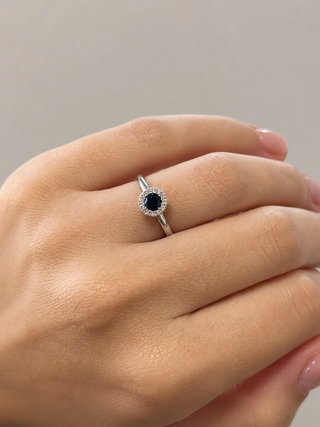 Silver ring with a black gemstone on a hand against a neutral background