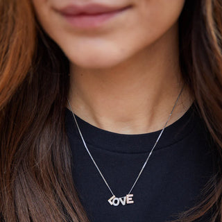 Person wearing a necklace with a 'LOVE' pendant on a black background