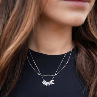 Person wearing a silver 'NAME' necklace on a black shirt