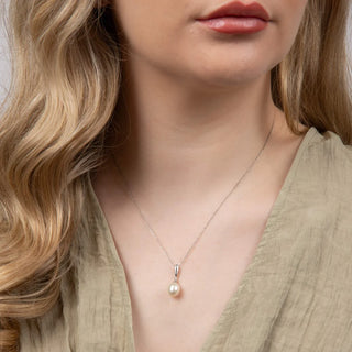 Close-up of a person wearing a pearl necklace with a neutral background