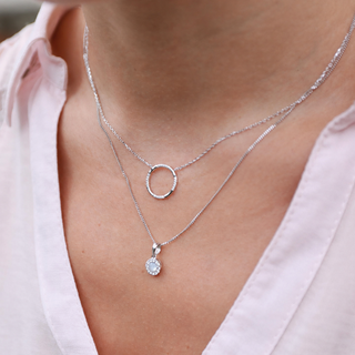 Close-up of a person wearing two silver necklaces with circular pendants.