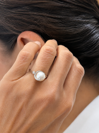 Close-up of a hand wearing a pearl ring with a blurred background
