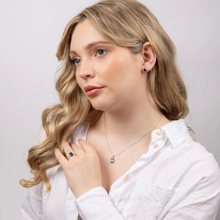 Woman wearing a necklace, ring, and earrings on a plain background