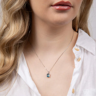 Necklace with a blue gemstone pendant worn by a person with blonde hair and a white shirt.
