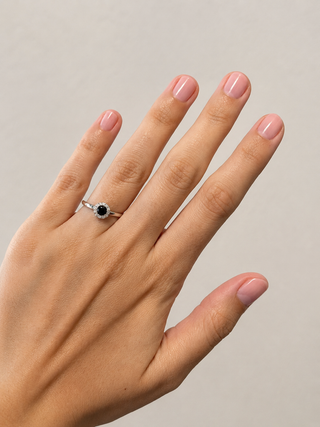 Hand wearing a ring with a black blue gemstone on a neutral background