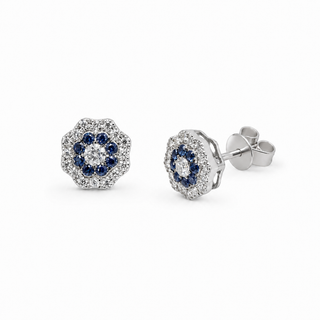 A pair of round cluster stud earrings in silver-tone metal, featuring a central round clear stone surrounded by a halo of small clear stones and a ring of deep blue stones, shown on a plain white background.