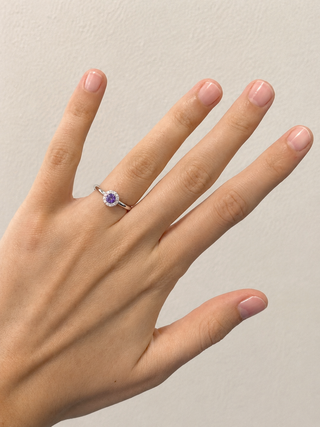 Hand wearing a ring with a purple gemstone on a neutral background