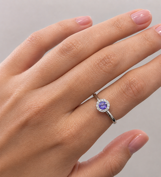 Silver ring with a purple gemstone on a hand against a gray background