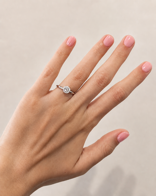 Hand wearing a diamond ring with pink nail polish on a neutral background
