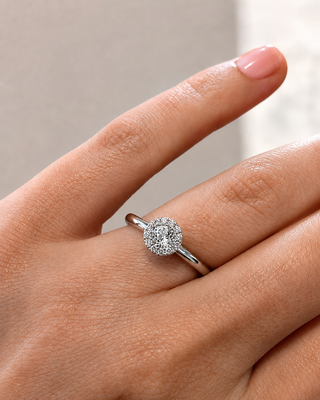 Close-up of a hand wearing a diamond ring on a neutral background