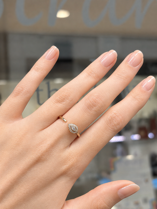 Hand wearing a gold ring with a diamond on a blurred indoor background