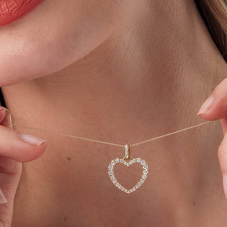 Heart-shaped diamond pendant on a gold chain held by a person.