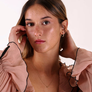 Woman wearing a light pink blouse with black trim, posing against a plain background.