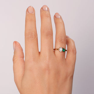 Hand wearing a ring with a green gemstone on a light background