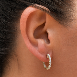 A close-up of a person's ear wearing a small gold hoop earring set with lab grown diamonds