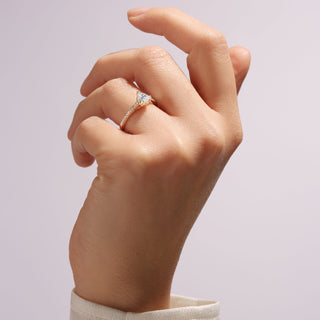 Hand wearing a gold ring with a diamond on a light gray background