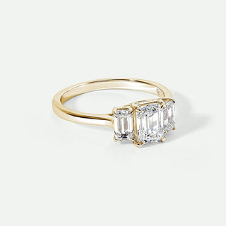 Gold ring with three emerald-cut diamonds on a white background