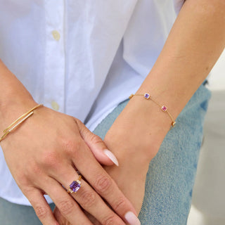 Close-up of hands wearing gold bracelets and a ring with a purple gemstone.
