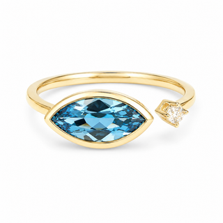 A gold ring featuring a marquise-cut light blue gemstone in a bezel setting and a small round clear accent stone on the band, shown on a plain white background.