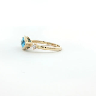 A yellow gold ring featuring a marquise-cut light blue gemstone and a small round-cut clear accent stone, set against a plain white background.