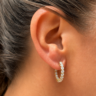 A close-up of a person's ear wearing a small gold hoop earring set with diamonds