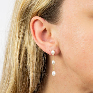 Close-up of a person wearing pearl drop earrings with a plain background