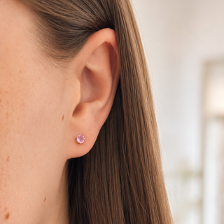 Close-up of a person wearing a pink stud earring with a blurred indoor background