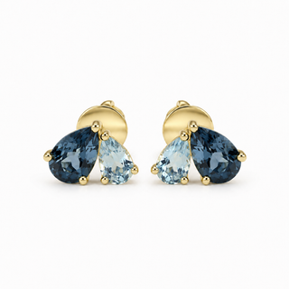 A pair of gold stud earrings featuring pear-shaped blue topaz and light blue topaz gemstones in a prong setting, shown against a plain white background.
