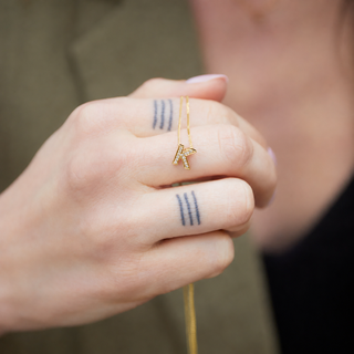 Gold necklace with a small pendant held by a hand with tattoos.