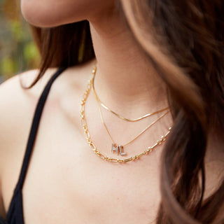 Close-up of a person wearing gold necklaces with letter pendants.
