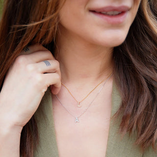 Person wearing a gold necklace with a small letter 'A' pendant, holding their hair.