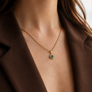 Gold necklace with a green gemstone pendant on a person wearing a brown blazer.