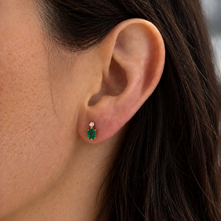 Close-up of an ear wearing a green emerald earring with a blurred background