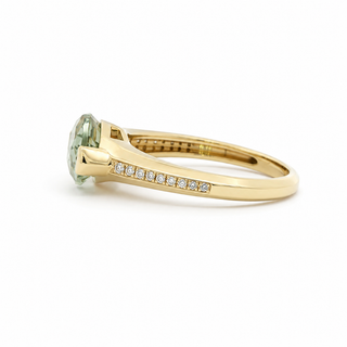A yellow gold ring featuring a round light green gemstone and a row of small clear stones along the band, shown on a plain white background.