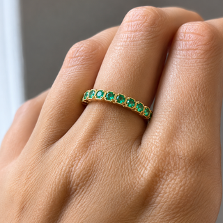 A close-up of a hand wearing a gold eternity ring set with round-cut green emeralds.