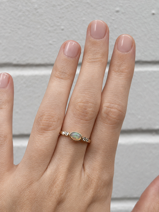 Hand wearing a gold ring with an opal stone against a neutral background