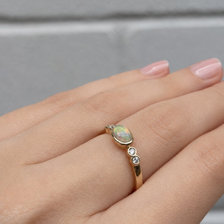 Gold ring with an opal stone on a hand against a gray background