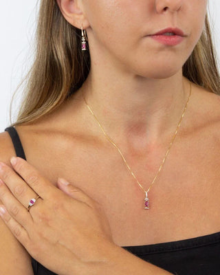 Woman wearing a gold necklace with a pink gemstone pendant, black top, and earrings.