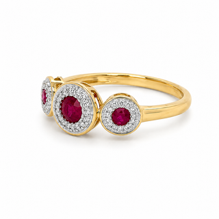 A yellow gold ring featuring three circular settings with deep red gemstones surrounded by small clear stones, shown on a clean white background.