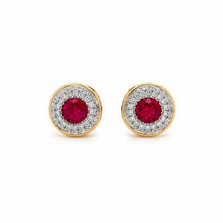 A pair of gold and white gold stud earrings featuring a round-cut pinkish-red ruby center stone surrounded by a halo of small clear stones, shown on a plain white background.