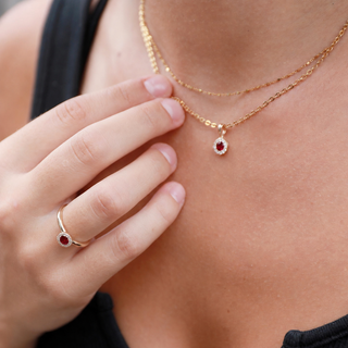 Close-up of a person wearing a gold necklace with a red gemstone pendant and matching ring.