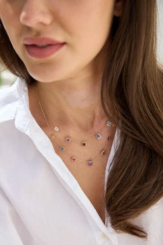 Close-up of a woman wearing a delicate necklace with small, colorful stones.