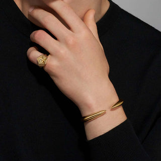 Gold bracelet and ring on a person's wrist against a black background